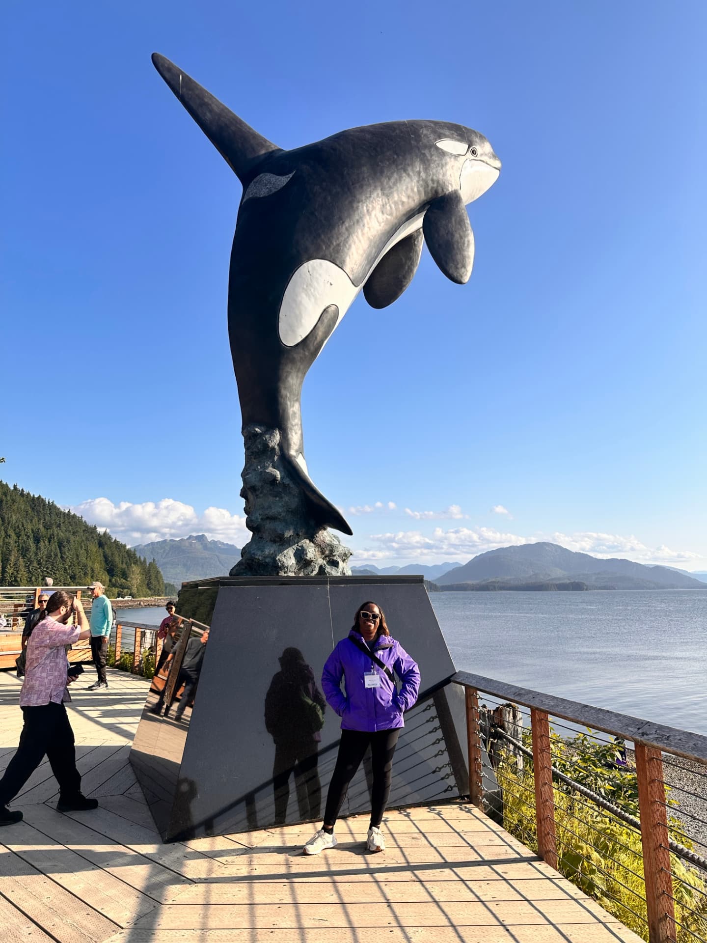 Melissa Odom beside the bronze breaching orca sculpture on the Icy Strait Point waterfront in Hoonah, Alaska