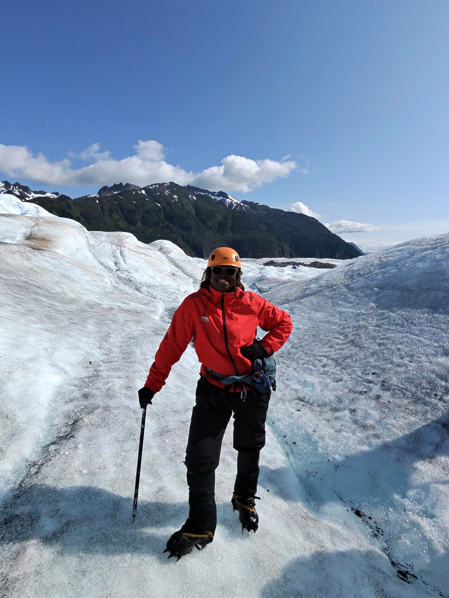 Melissa Odom in a red shell jacket, helmet and crampons standing on the blue ice of Mendenhall Glacier near Juneau, Alaska