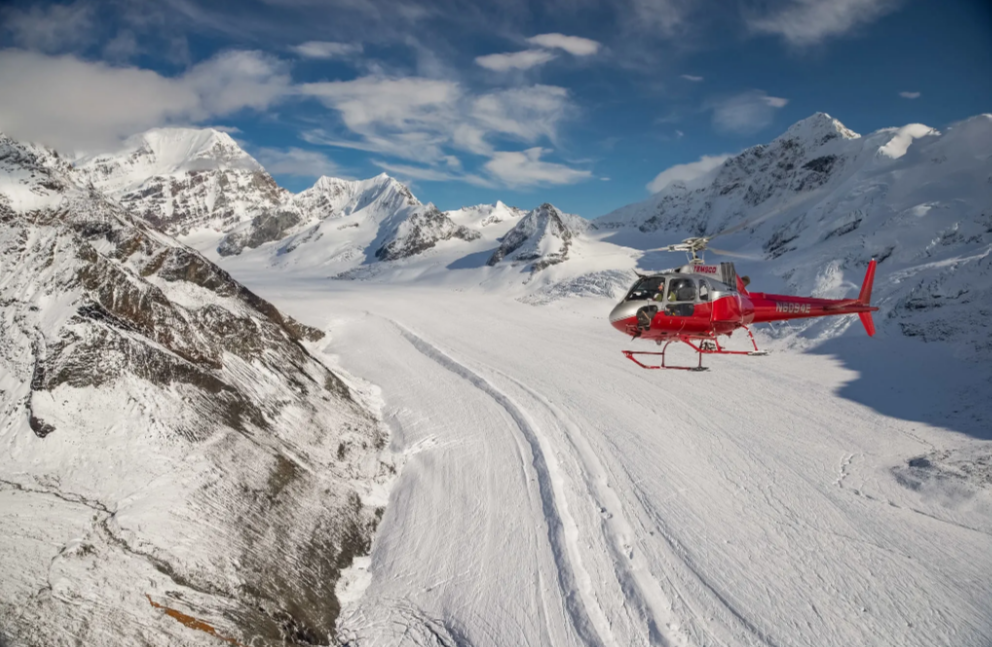 A helicopter flying over a snow-covered glacier in Alaska